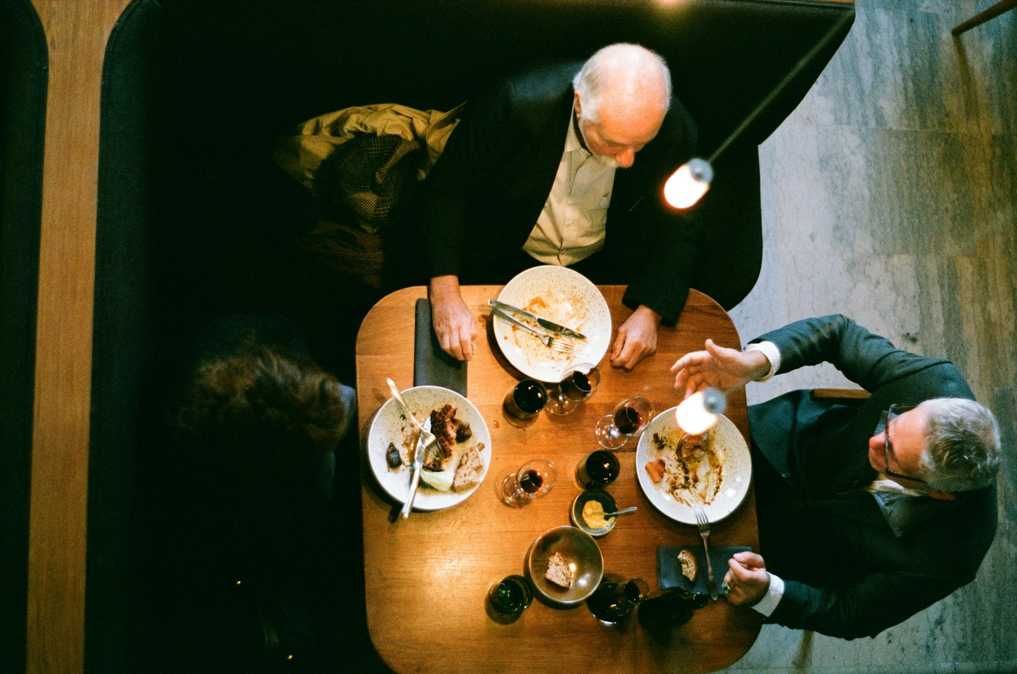 Une table vue de dessus, de nuit : assiettes, verres et mains de convives dans la pénombre